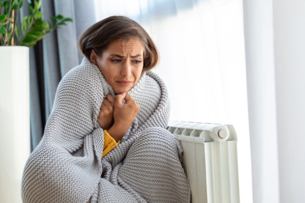 Woman sitting beside the radiator Feeling Cold At Home due to HVAC system neglect